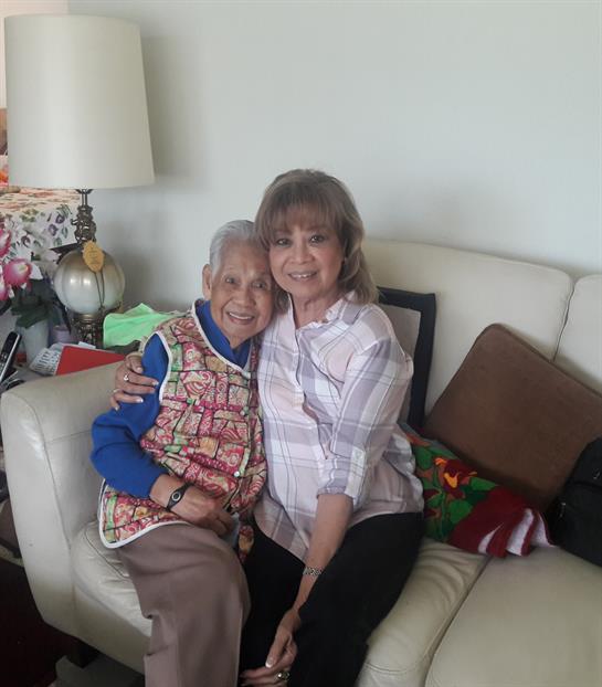 Grandmother and granddaughter share a joyful embrace while relaxing together on a couch.