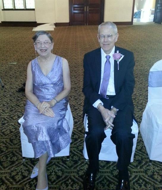 Couple in formal attire sits together, smiling at a celebration in a decorated venue.