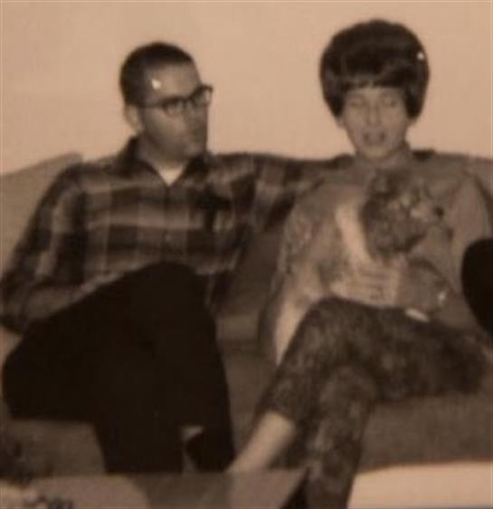 A couple sits together on a couch, enjoying a quiet moment with their pet cat in the 1960s.