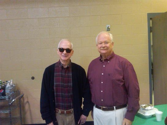Two men stand side by side, smiling and enjoying their time at a local gathering.