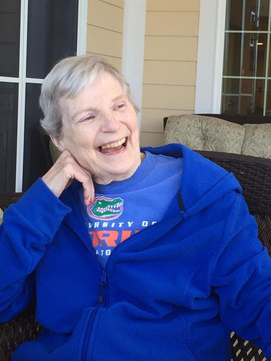 Elderly woman laughs heartily while relaxing on a porch during a sunny spring day.