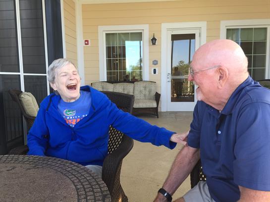 Two seniors share a joyful moment on a porch, laughing and enjoying each other's company.