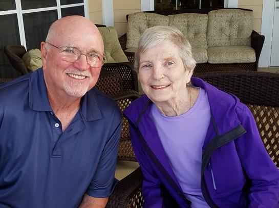Two elderly individuals share a joyful moment on a cozy porch while wearing casual clothes.