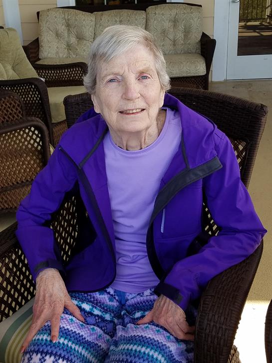 Senior woman enjoys the sunlight while sitting comfortably in an outdoor chair, smiling cheerfully.