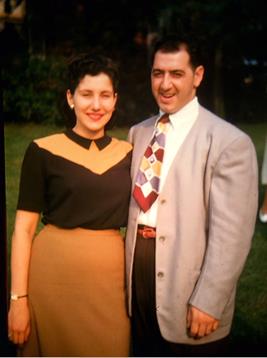 A smiling couple poses together in vintage attire during a bright outdoor gathering.