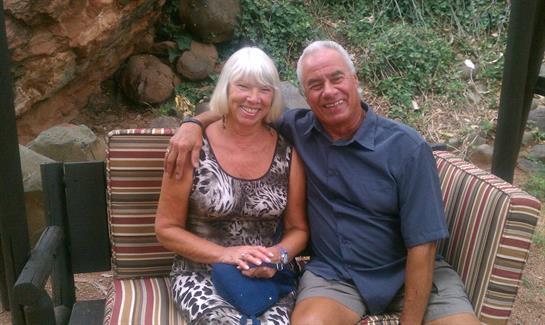 Two people sit closely together, smiling and enjoying each other's company in a lush environment.