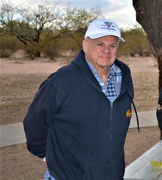 Man in a jacket and cap is outdoors in a sunny desert environment surrounded by sparse vegetation.
