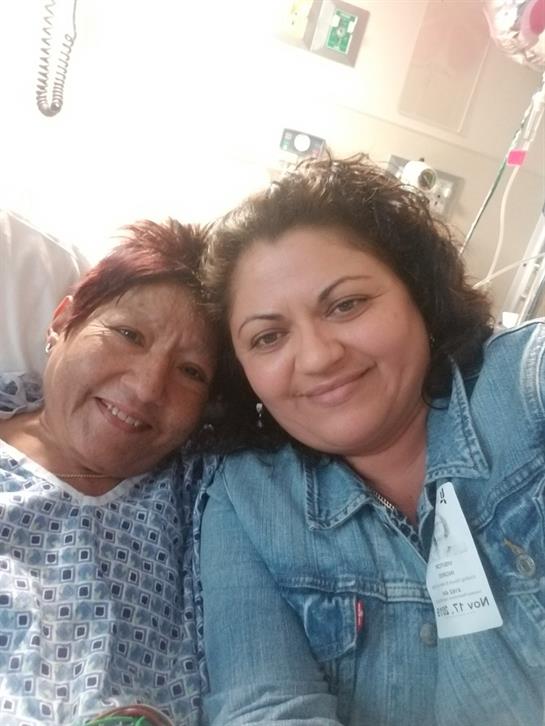 Two women smile warmly while sitting together in a hospital room, showcasing love and support.