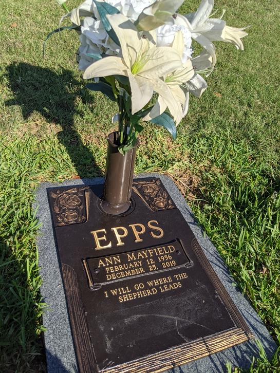 A grave marker displays a tribute with flowers placed lovingly, surrounded by green grass.