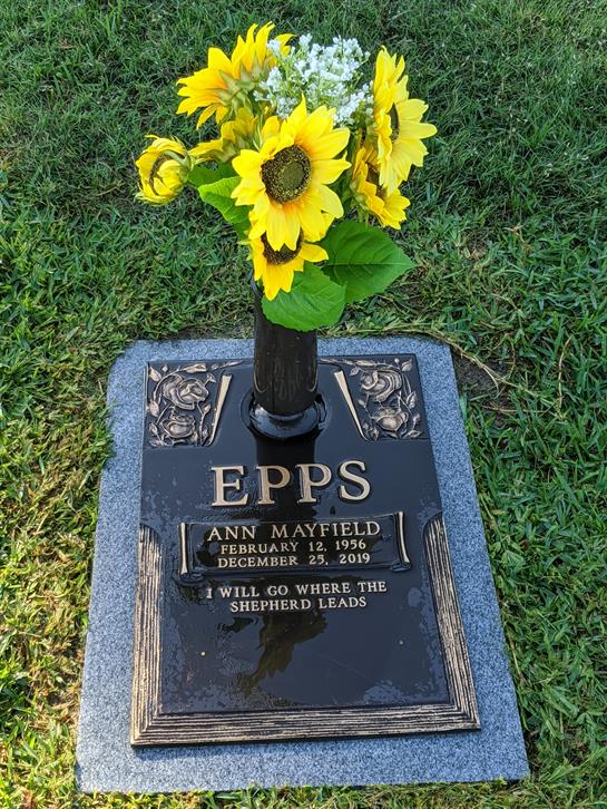 A peaceful grave marker featuring bright sunflowers, commemorating Ann Mayfield's life.