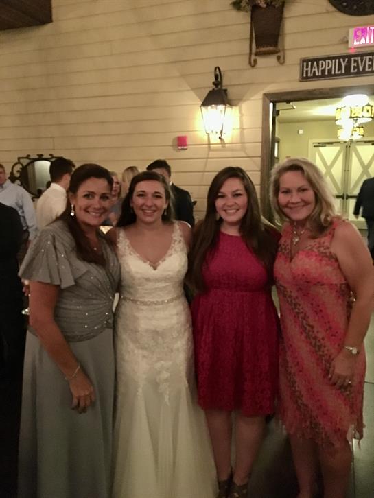 Four friends happily pose at a wedding, showcasing their elegant outfits and smiles.