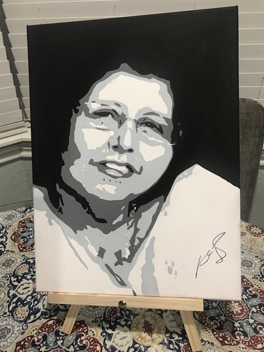 A woman with glasses is smiling in a black and white portrait displayed on an easel indoors.