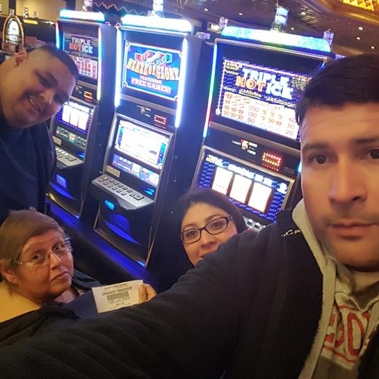 Four friends gather together, taking a selfie while playing slot machines at a busy casino.