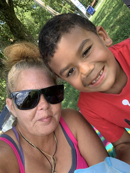 A woman and a young boy sit together, smiling happily in a park under the sun.