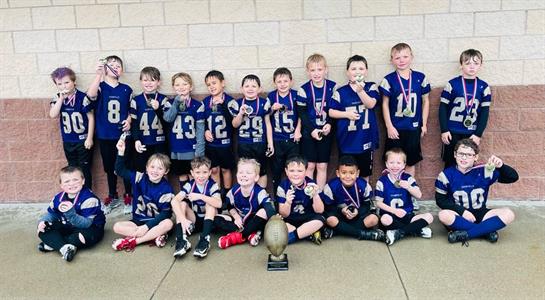 Group of young football players show off medals and a trophy after winning their tournament.