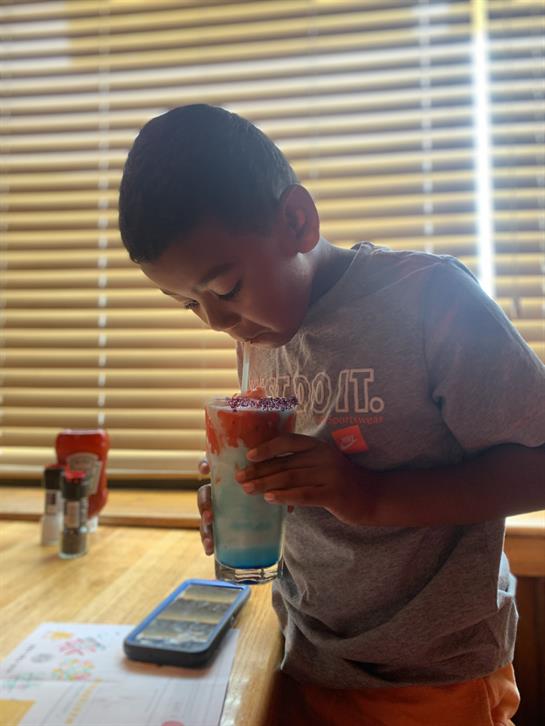 A child is savoring a vibrant beverage, focused on his drink in a sunlit room.