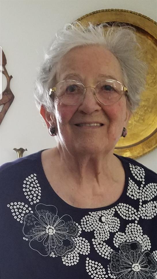 A joyful elderly woman is smiling in a bright indoor environment filled with decor.