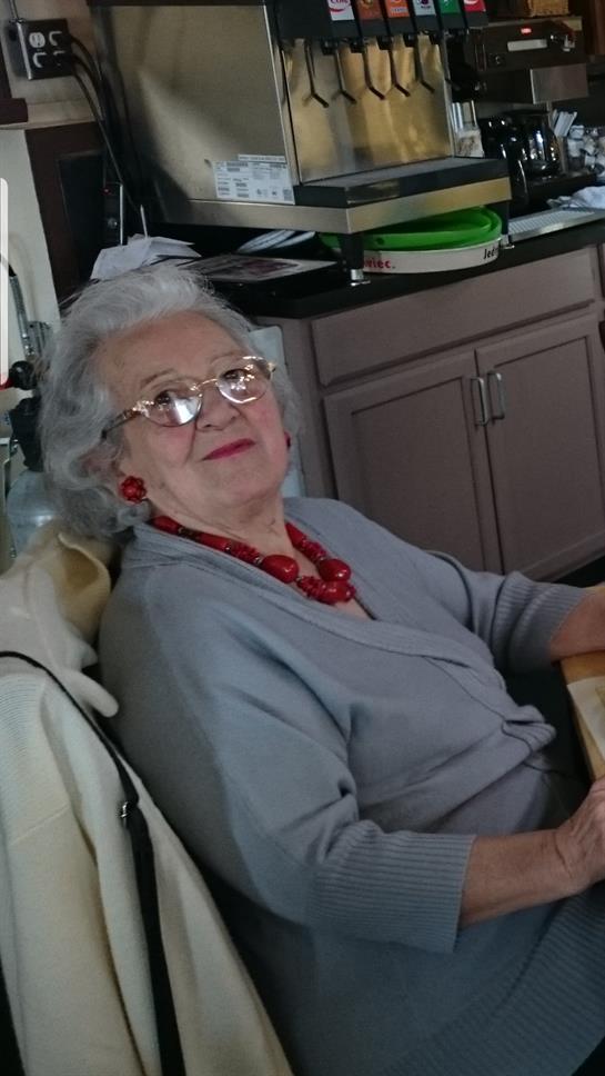 Senior woman at home, wearing glasses and a bright red necklace, smiles joyfully.