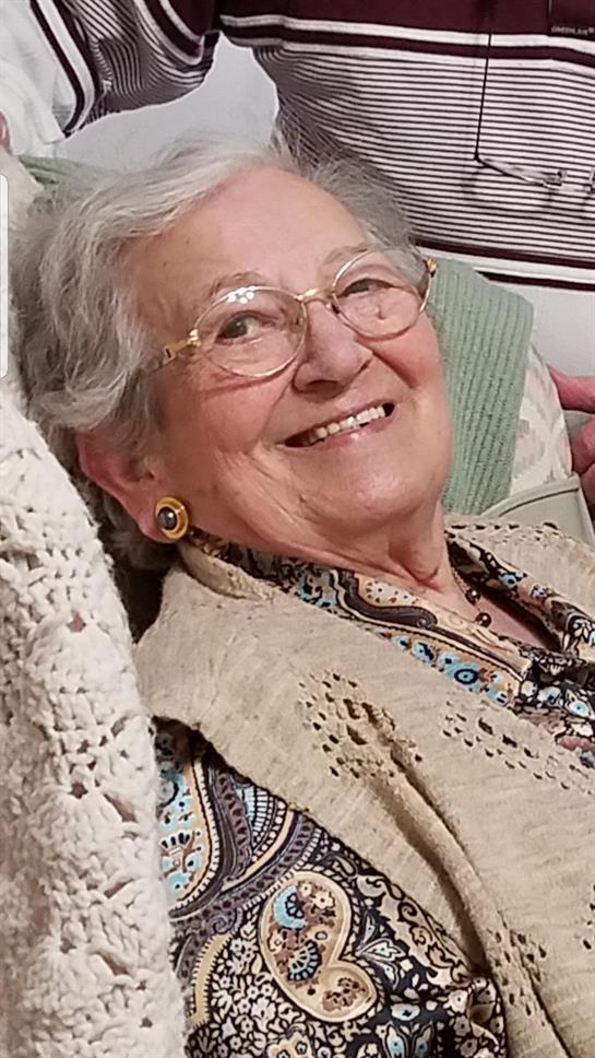 An elderly woman smiles brightly while relaxing in a comfortable chair with a crochet throw.
