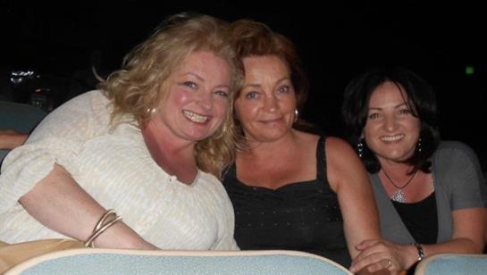 Three women appear cheerful and relaxed while celebrating at a social event under the night sky.