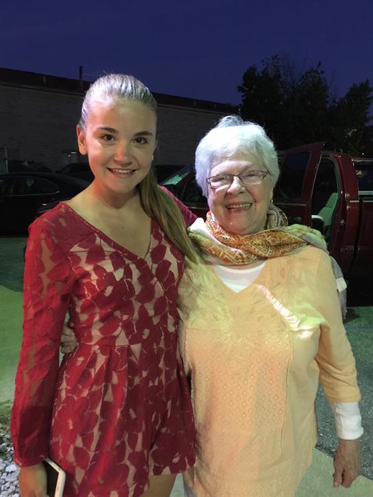 A young woman in a red dress stands beside an elderly woman in a yellow outfit at dusk.