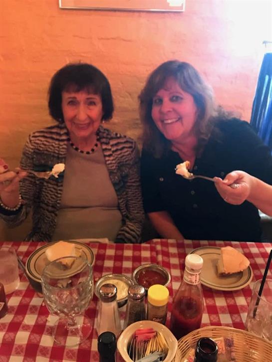 Two women happily pose with dessert at a restaurant, showcasing their delight and friendship.