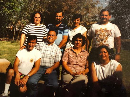A cheerful group of nine friends sits on a bench in a park, sharing smiles and laughter together.