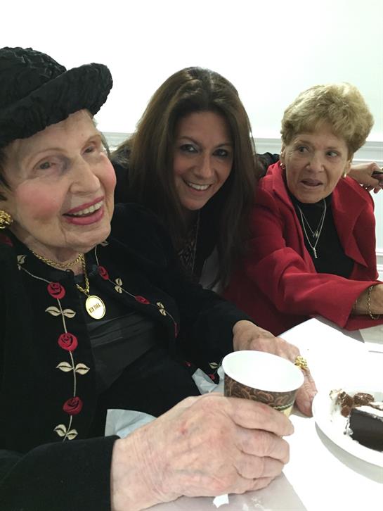 Three women smile and share stories while enjoying snacks and drinks during a social gathering.