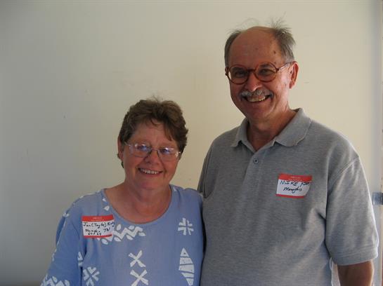 Two friendly individuals stand together, both looking joyful and engaged in conversation.