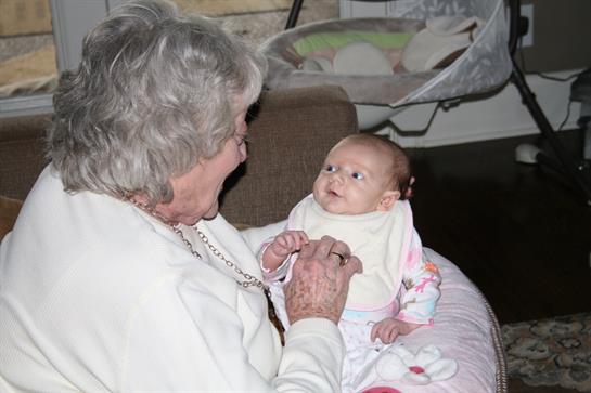 A grandmother engages with her baby granddaughter, both smiling and enjoying their time together.