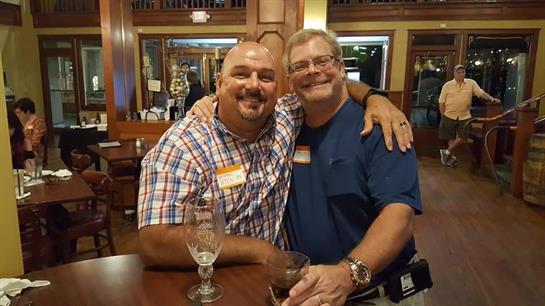 Two friends happily embrace while enjoying drinks at a bar during a cheerful evening.