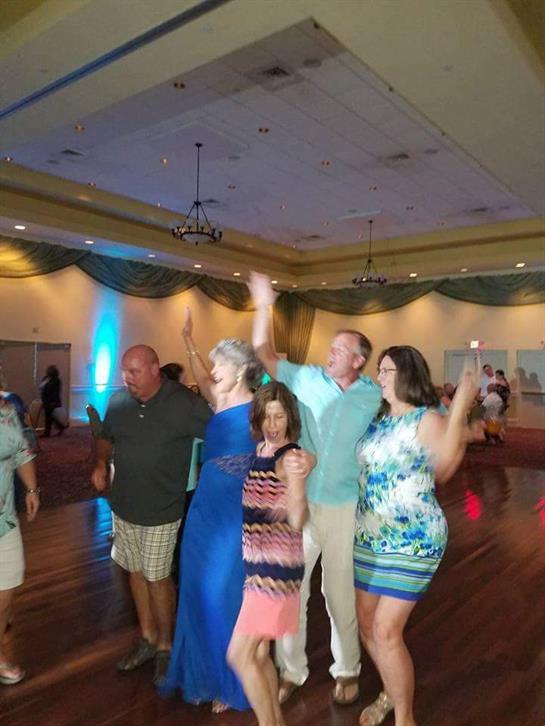 Friends joyfully dance at a social event, wearing vibrant outfits and smiling brightly.