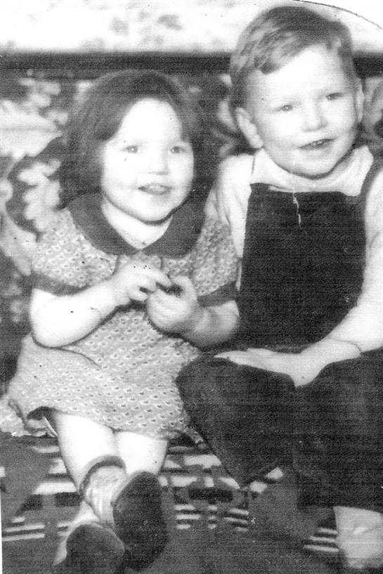 Two smiling children are enjoying each other's company, surrounded by floral decor.