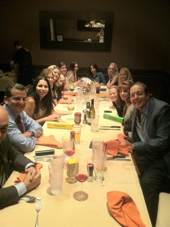 Friends gather around a long table, enjoying drinks and lively conversation at dinner.