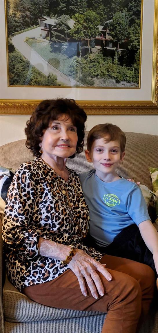 A happy grandmother poses with her grandson on a comfortable couch in their cozy living room.