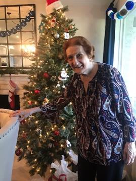 An elderly woman joyfully arranges ornaments on a beautifully decorated Christmas tree.