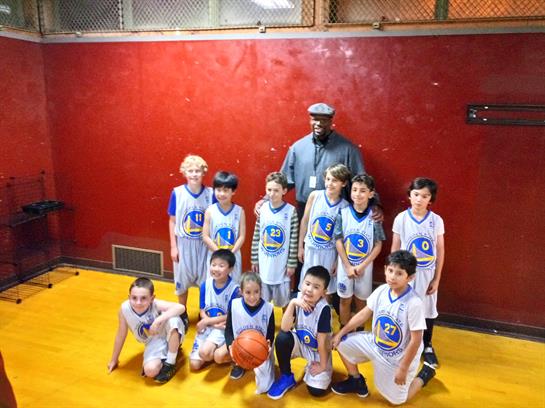 Young basketball players smile together with their coach in a vibrant gym setting.