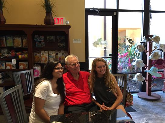 Two smiling women sit beside an older man in a cozy cafe, enjoying a joyful moment.