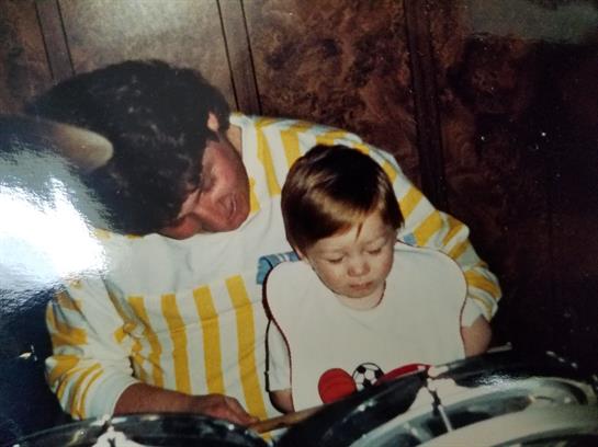 A father and young child engage in a joyful moment while playing the drums together.