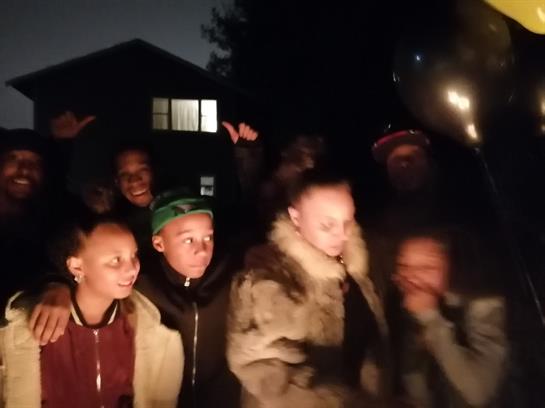Children joyfully gather at night by a house, sharing laughter and excitement.