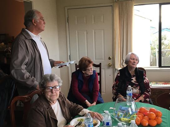 Seniors share food and laughter around a dining table in a warm room filled with joy.