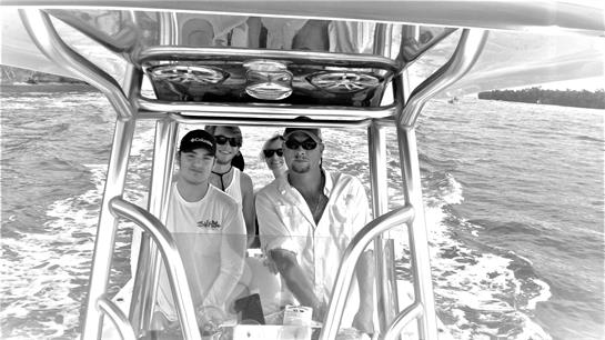 Four friends relax on a boat, navigating clear waters under bright sunlight.