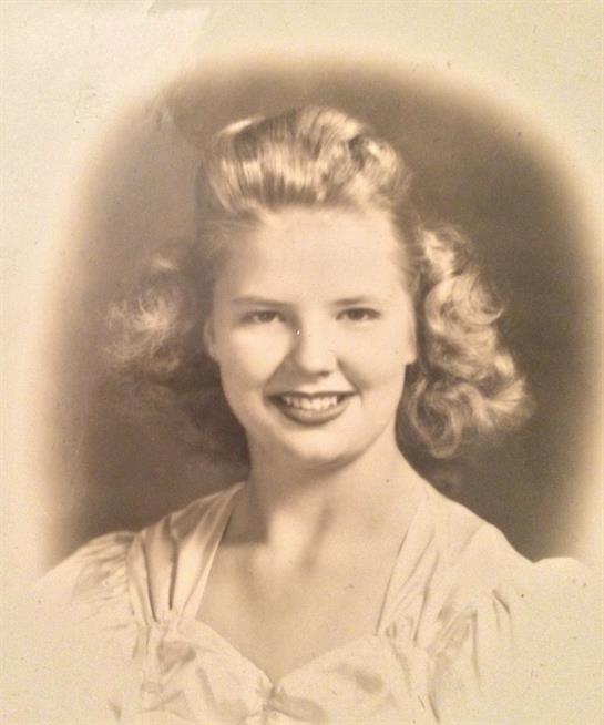 A young woman with curled hair beams in a classic portrait, showcasing 1940s fashion and style.