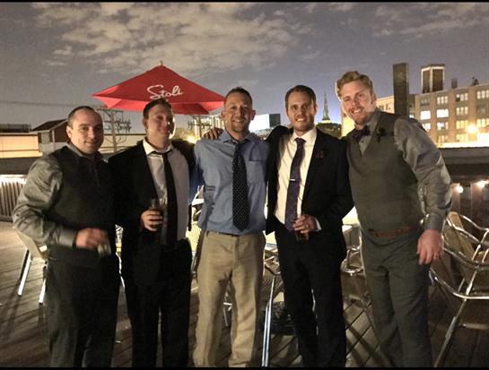 Friends dressed in formal wear enjoy a lively night on a rooftop overlooking the city.