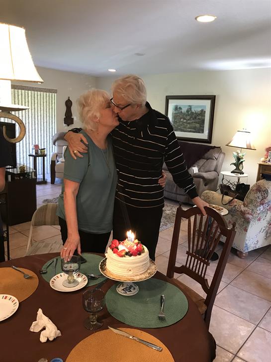 Joyful celebration as an elderly couple shares a sweet kiss near a cake in their home.