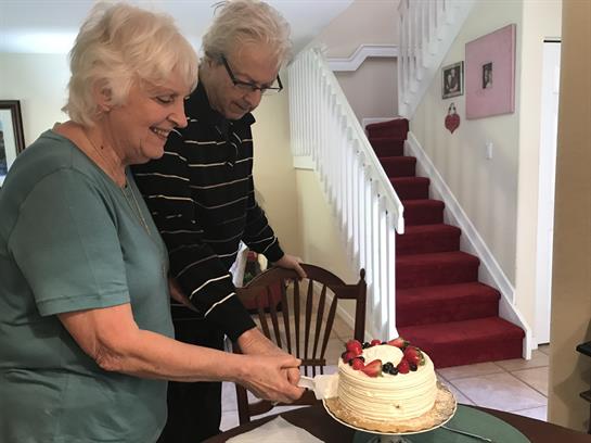 A happy couple cuts a cake together in their home, celebrating a special occasion with smiles.