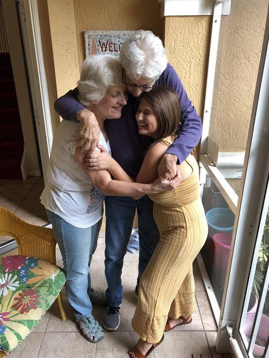 Three family members of different generations joyfully hug each other at home, celebrating together.