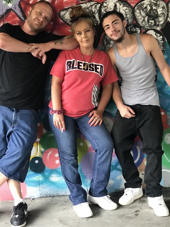 Three friends gather and pose in front of a vivid mural, enjoying a sunny day together.