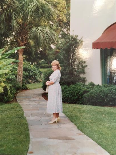A woman dressed in a light-colored dress stands gracefully on a stone pathway in a garden.
