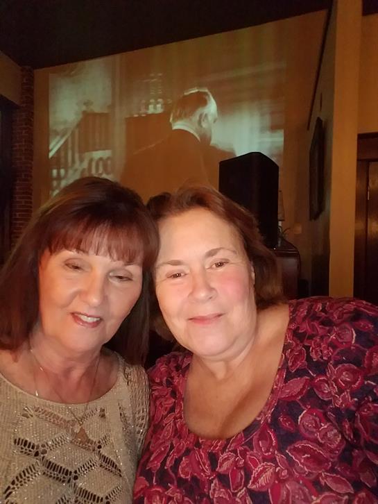 Two friends smile warmly while enjoying their time at a lively venue with vintage decor.